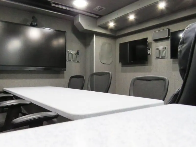 A conference room in the City of Coral Gables with six office chairs around a white table, multiple wall-mounted screens, and grey walls with overhead lighting—perfect for Mobile Command meetings.