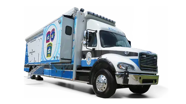 A large white and blue Mobile Command police vehicle with official Coral Gables city logos on the side is parked, viewed from the front left corner against a solid black background.