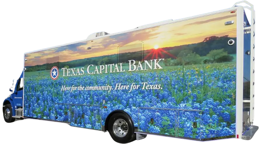 A large mobile bank vehicle with a Texas Capital Bank logo, covered in an image of bluebonnet flowers and a sunrise. Text reads: Here for the community. Here for Texas.