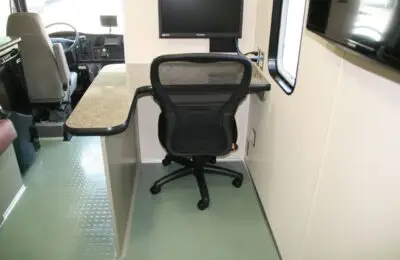 A mesh office chair sits at a desk with a marble-like surface inside a vehicle, with a computer monitor on the desk and the drivers seat visible in the background. Women’s Center for Radiology
