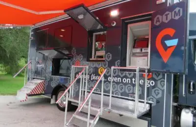 A mobile banking truck featuring an ATM and service windows is parked outdoors. The truck has stairs leading up to entrances, branded signage, and is positioned near grass and trees. Granite Credit Union