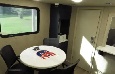 A small meeting area with a round table and four chairs, a window showing green grass outside, a door, cabinets, a printer, and a wall-mounted keypad—perfect for private consultations in a Family Advantage Federal Credit Union office.