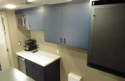 A kitchenette area with blue cabinets, a white countertop, and modern appliances offers convenience at Family Advantage Federal Credit Union; an office-style chair is visible through an open doorway.