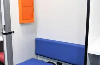 A small room with a blue cushioned bench, an orange wall-mounted file holder, and a partial view of a desk and chair in the background.