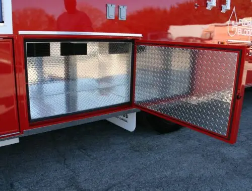 A red vehicle with an open side compartment showing an empty, metal, diamond-plate storage area. Part of a logo reading Floridas Blood Centers is visible on the upper right.