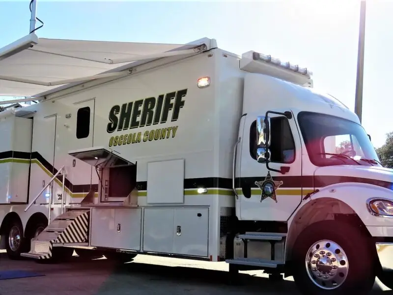 A large white Volusia County Sheriffs Office Public Safety Vehicle labeled Sheriff Osceola County is parked outside in daylight, with an awning extended and compartments open on its side.