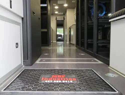 Interior view of a mobile command vehicle with a clean aisle, storage compartments, and a floor mat that reads MBF Industries 407-339-0414 near the entrance.