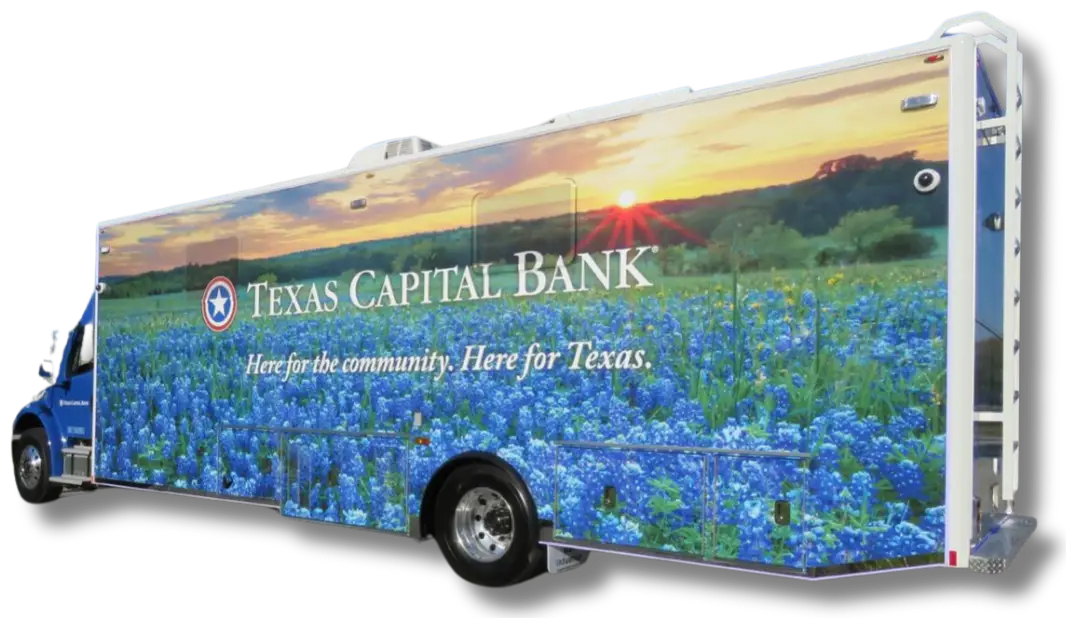 A large bus wrapped with an image of a bluebonnet field at sunset, proudly featuring Texas Capital Bank’s logo and the message: Here for the community. Here for Texas.