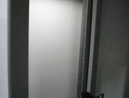 A small, private restroom area with a closed door and a white toilet partially visible at the bottom, illuminated by a ceiling light.