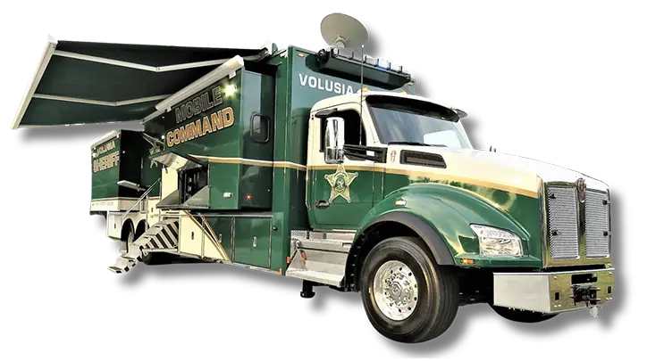A large green and white Volusia County Sheriffs Office Public Safety Vehicle labeled Mobile Command, featuring sheriffs department markings, an extended canopy, satellite dish, and steps leading to an open side door.