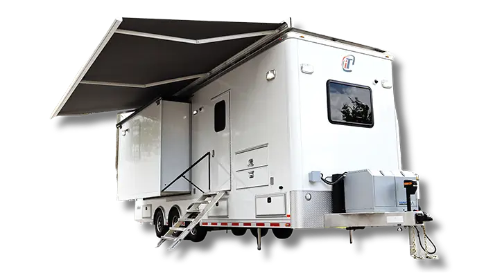 A white mobile trailer with double axles, side stairs, a large extended awning, and an attached external generator unit is shown against a plain background—perfect for ATL-Fulton County events or projects.